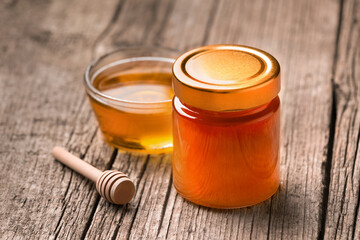 Honey in a jar and in a bowl, a wooden dipper on a wooden background, close-up.