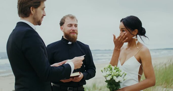 Wedding on the seashore, the groom reads the oath from a piece of paper, the bride wipes her tears