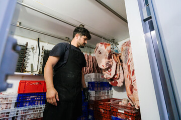 Serious man standing in meat drying room in butchery