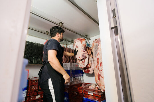 Male worker hanging meat pieces for drying in butchery