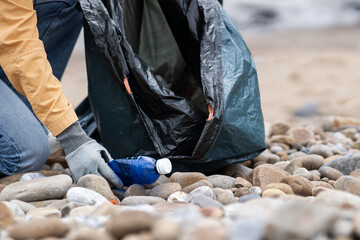 Person picking up plastic at beach.