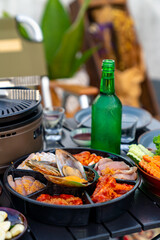 Korean food barbecue grill and alcohol drink vodka on the table. Asian people enjoy celebration meeting dinner party eating bbq grill and drinking Korean vodka at outdoor rooftop on summer vacation.