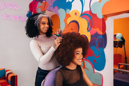 Cheerful latin hairdresser cutting afro hair to a client