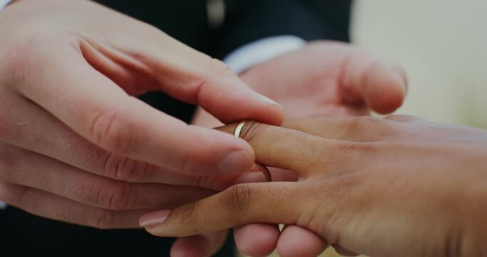 The groom puts a ring on the bride's finger, standing outdoor, close-up of hands