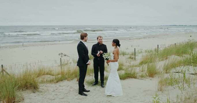The bride and groom kiss standing in front of the priest on the seashore