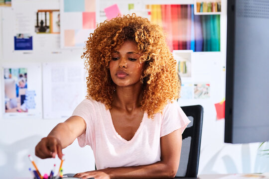 Worker takes pencil at desk.
