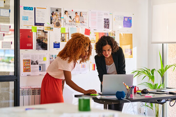 Two businesswomen use laptop in office.