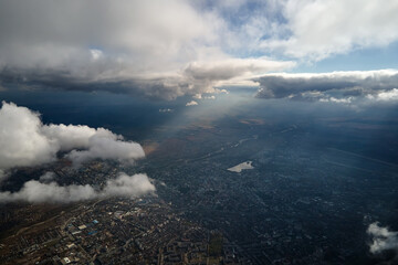 Aerial view from airplane window at high altitude of distant city covered with white puffy cumulus...