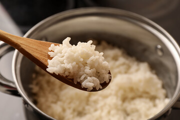 Wooden spoon with delicious rice over pot, closeup