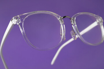 Stylish pair of glasses on purple background, closeup
