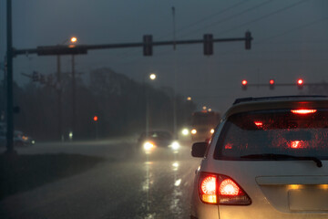 Cars driving at rainy night at traffic lights on american wide road intersection in city area. Transportation system in USA