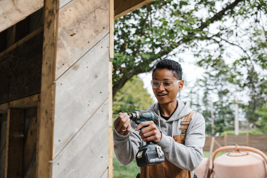 Woman carpenter using power drill on building project.