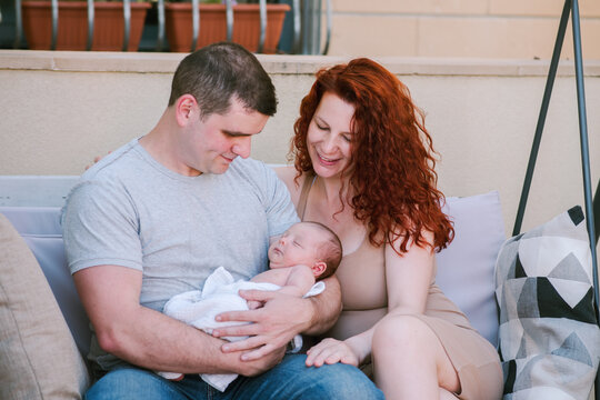 Young Couple, New Parents, Lovingly Admire Their Baby.