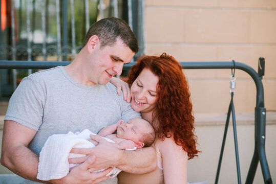Young Couple, Newly-Made Parents, Look with Love at Their Child.