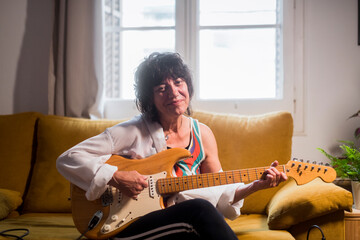 Smiling woman playing guitar at home looking at camera