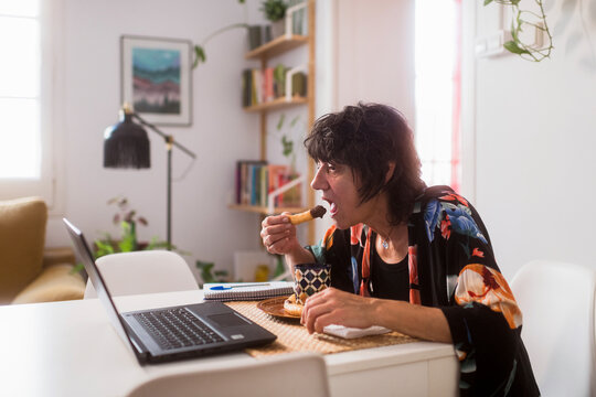 Woman having breakfast in front of laptop at home