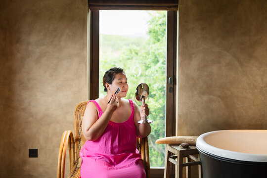 Curvy woman applying with brush clay mask on face