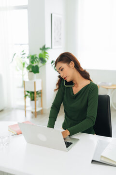 Happy young woman sitting at her desk working and answering on phone