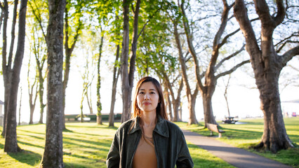 A young woman stands near a tree, looking at the camera.