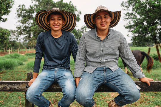 Two young Colombian cowboy brothers casually seated on a fence