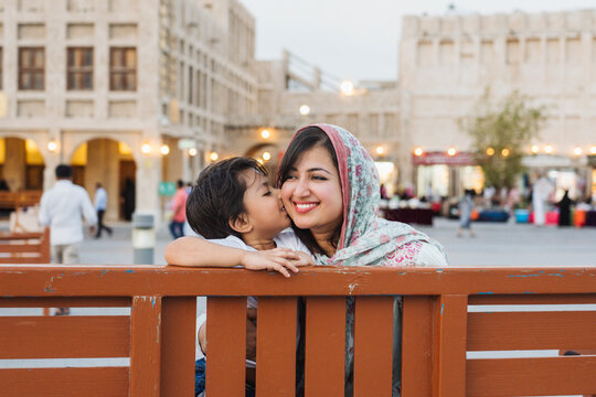 Cute boy kissing Indian mother on bench