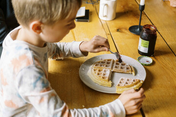 boy sitting at breakfast table eating a waffle with jam