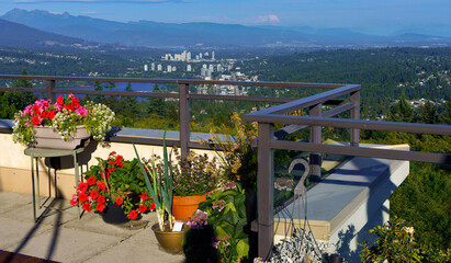 Bright summer flowers in planters on patio overlooking Burrard Inlet and Fraser Valley with mountains in silhouette in background
