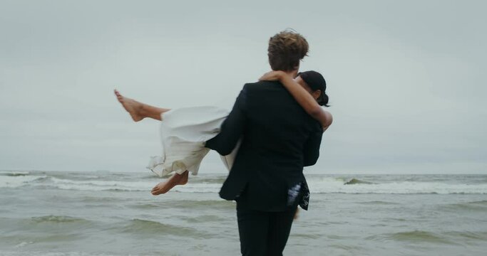 The groom takes the bride in his arms and spins with her, standing on the seashore