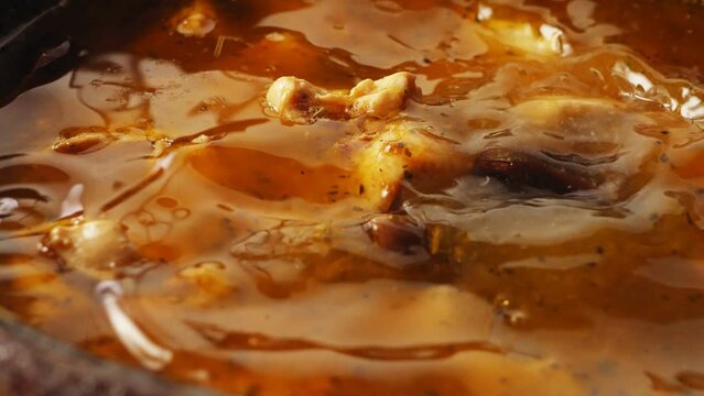 Pieces of chicken fried in a cast-iron skillet in oil with onions and spices in the broth where the dates fall. Close-up