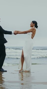 The bride and groom are spinning holding hands, and then kissing and hugging standing on the seashore