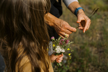 little girl with long hair picking flowers outdoors with grandma