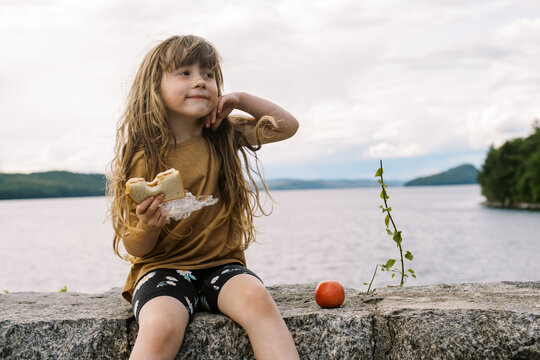 little girl sitting on rock wall overlooking a lake to eat lunch 