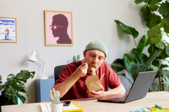 Male designer having noodles at desk in studio