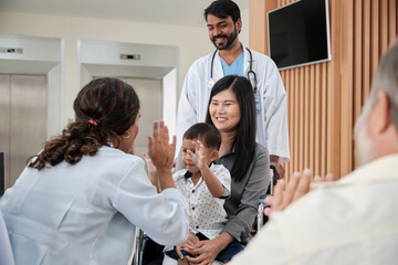 Happy young female pediatric doctor in uniform teasing little boy in wheelchair for medical exam at...