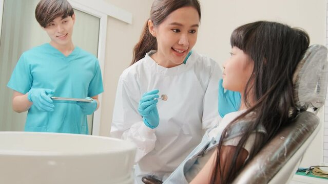 Asian female pediatric dentist and assistant check and examination a little girl's caries teeth in dental clinic, well-being hygiene, and professional orthodontic healthcare work in kid hospital.