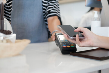 Female customer holding phone near nfc terminal make contactless mobile payment.