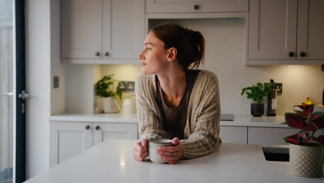 Portrait of young woman taking a break with cup of coffee leaning on kitchen counter at home - shot in slow motion