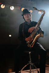 Friendly man musician sitting on chair with saxophone in his hand and looking at camera