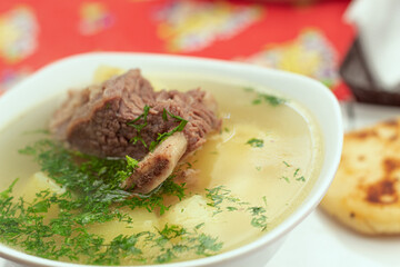 Close up of a bowl of hot soup with a piece of meat in the middle and some coriander. Rib broth with a small arepa. Concept of traditional Colombian food.