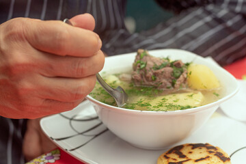 Close up of a man's hand eating a bowl of soup. Meat broth, cilantro and potato accompanied with a small arepa. Man having lunch. Concept of traditional Colombian food.