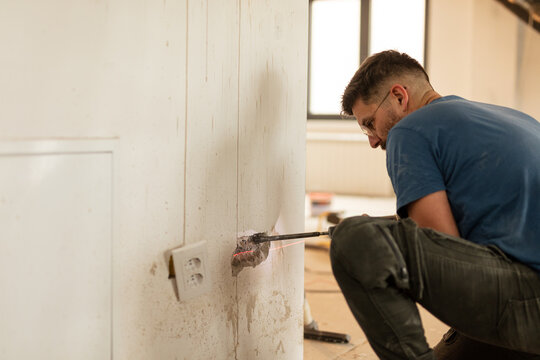Electrician drills a hole in the wall for an electrical outlet