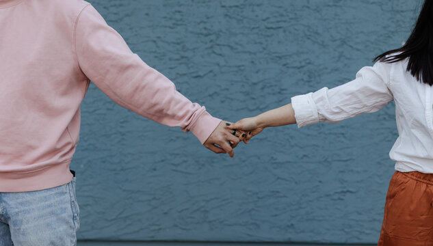 Anonymous couple holding hands and pulling apart with blue wall 