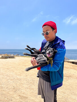 A man holding a black dog in his arms in front of a empty beach