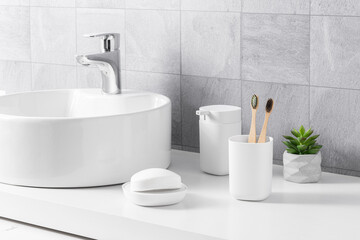Modern bright bathroom interior with a white sink, bamboo toothbrushes, and a grey color porcelain...