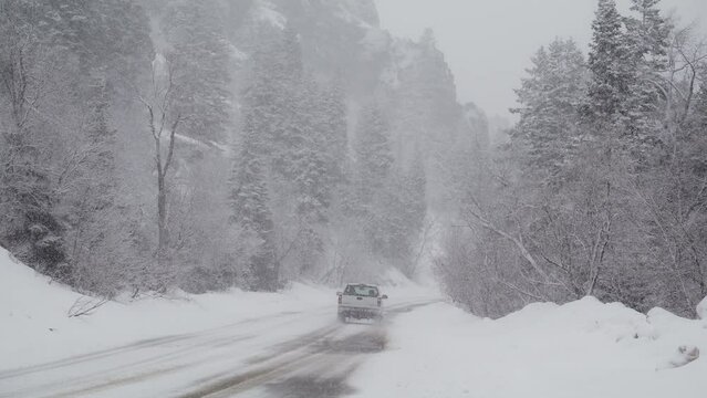 Rear view panning shot of truck driving on snow covered road near trees / American Fork Canyon, Utah, United States