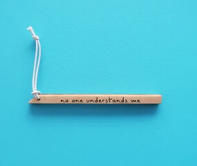 Wood piece on copy space blue background with handwritten text NO ONE UNDERSTANDS ME, concept of...