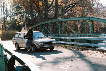 millennial man standing by his old classic car outdoors in autumn