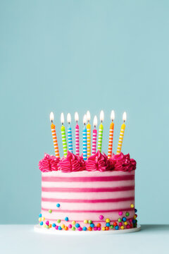 Pink striped birthday cake with lots of birthday candles