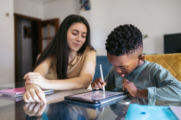 Girl babysitting a primary school boy doing his homework with a tablet