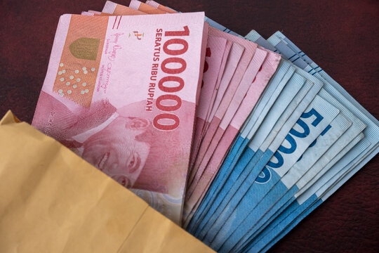 row of Indonesian rupiah banknotes in a salary envelope, on a brown and maroon leather sova
